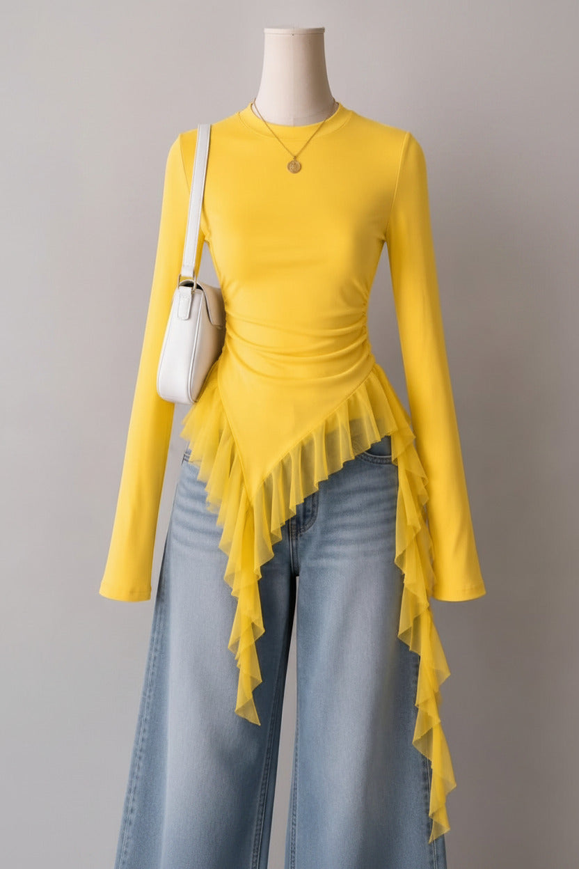 Mannequin wearing a yellow long-sleeve top with ruffled details and light blue jeans, against a neutral wall with decor.