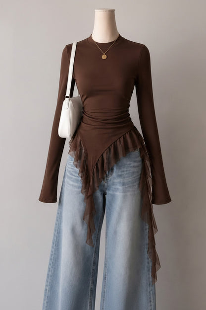 Mannequin wearing a brown top with ruffled details and light blue jeans, against a neutral wall with framed pictures.